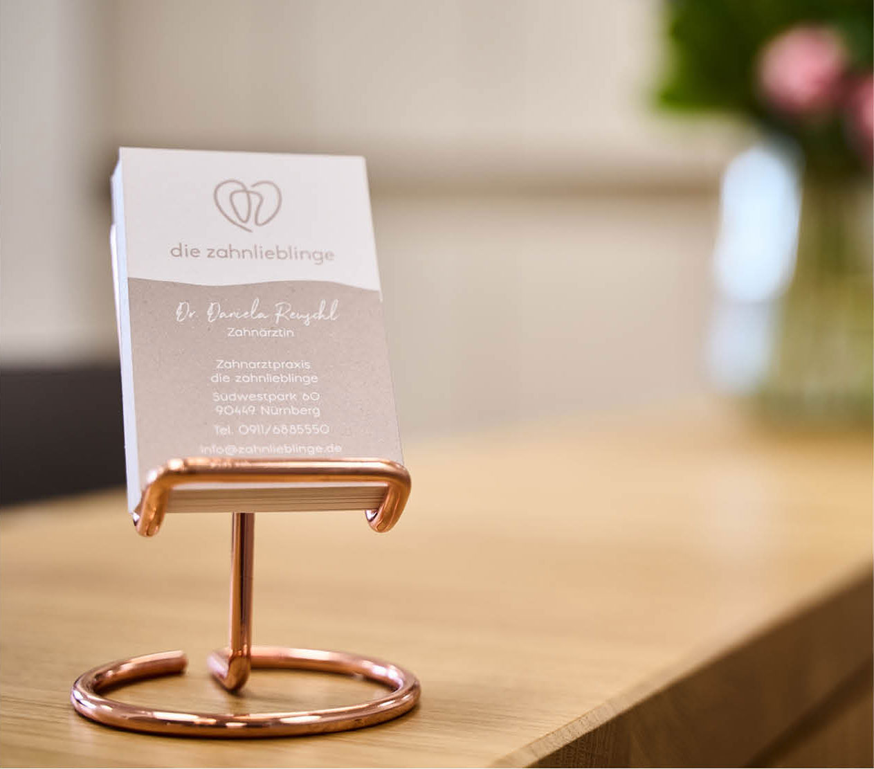 Ein Flyer der zahnlieblinge steht in einem rosegoldenen Metallständer auf dem Empfangstresen der Zahnarztpraxis im Südwestpark Nürnberg