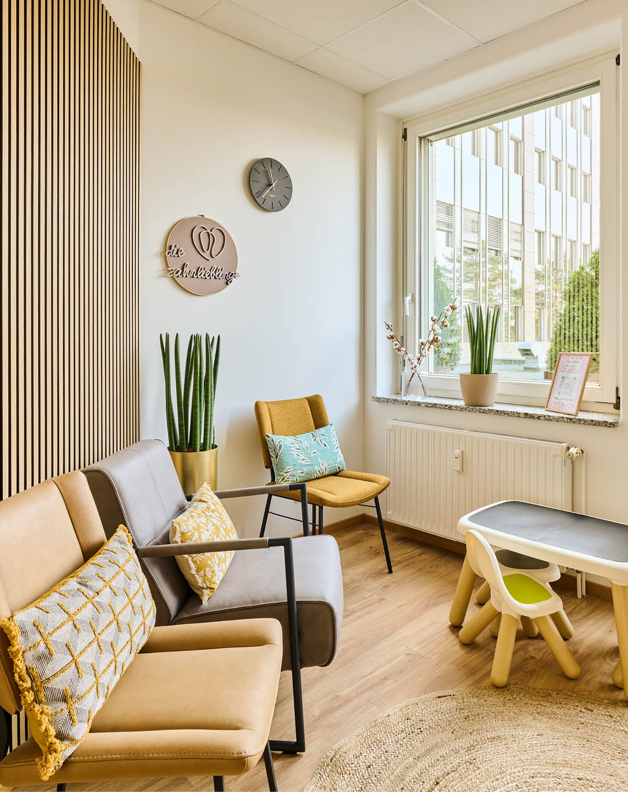 Das Wartezimmer der Zahnarztpraxis Zahnlieblinge mit gemütlichen Stühlen in gelb und grau sowie einer Spielecke für die kleinen Patient*innen.